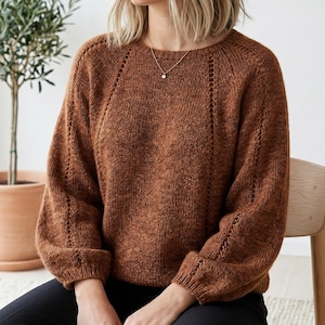 May include: A brown knit sweater with a round neckline and long sleeves. The sweater has decorative stitching along the sleeves and shoulders. The sleeves are cuffed at the wrists. The sweater is made of a soft, textured yarn.