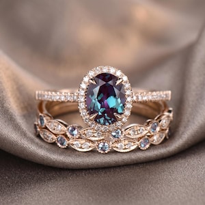May include: A rose gold ring set featuring an oval-cut, color-changing alexandrite gemstone surrounded by a halo of small diamonds. The set includes a matching band with small diamonds and a decorative band with leaf-like accents.