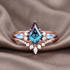 Puede incluir: Un juego de anillos de compromiso de oro rosa con una piedra preciosa de color turquesa en forma de cometa como pieza central. El anillo está flanqueado por piedras preciosas blancas más pequeñas y una banda curva con piedras blancas adicionales. Se incluye un segundo anillo.