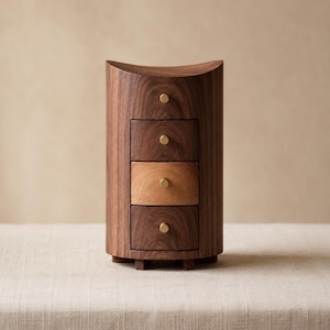 May include: A vertical wooden storage chest with a curved front and four stacked drawers. The unit is crafted from dark brown wood, with one drawer featuring a lighter tan wood finish. Each drawer has a small, round, gold-colored metal knob.