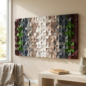 Op de afbeelding: Een groot, rechthoekig houten wandkunstwerk. Het kunstwerk bestaat uit talrijke kleine, vierkante blokken in verschillende tinten bruin, wit, grijs en groen, waardoor een gestructureerd, driedimensionaal effect ontstaat. Het stuk is aan een beige muur bevestigd.