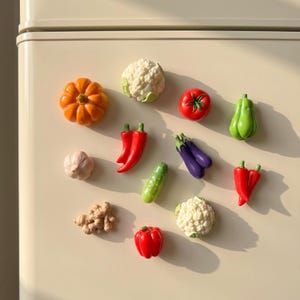 Può includere: Una collezione di dodici magneti da frigorifero a forma di verdura che include una zucca, un cavolfiore, un pomodoro, un peperone verde, aglio, peperoncini rossi, una melanzana, un cetriolo, zenzero e un peperone rosso su una superficie color crema.