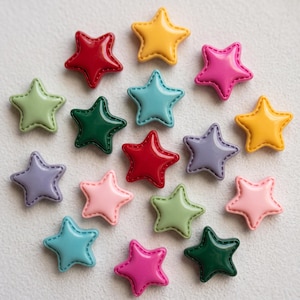 May include: A collection of seventeen star-shaped buttons in various colours including red, yellow, pink, light green, dark green, light blue, and lavender. Each button features a smooth, glossy finish with a stitched border detail along the edges.