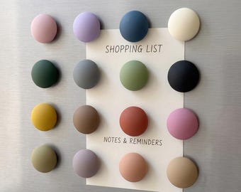 Puede incluir: Un conjunto de dieciséis imanes circulares con acabado mate en varios colores, incluyendo rosa, morado, azul, crema, verde, gris, amarillo, marrón, terracota y negro. Un papel blanco rectangular con el texto SHOPPING LIST y NOTES & REMINDERS.