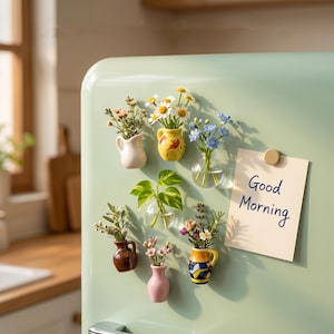 May include: A collection of miniature magnetic vases attached to a light green refrigerator. The set includes ceramic pitchers, glass bulbs, and colorful pots holding various small flowers and green leaves, alongside a note reading Good Morning.