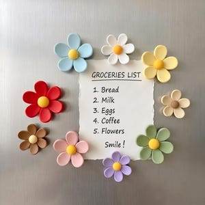 以下が含まれることがあります： GROCERIES LIST、1. Bread、2. Milk、3. Eggs、4. Coffee、5. Flowers、Smile!と黒い文字で書かれた白い紙の買い物リスト。その周りを青、白、黄、赤、茶、ピンク、紫、緑、ベージュの9つのカラフルな花型マグネットが囲んでいる。