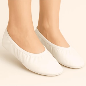 Könnte beinhalten: Ein Paar weiße Ballerinas. Die Schuhe sind aus einem weichen Material gefertigt und haben eine runde Spitze und einen flachen Absatz. Die Schuhe sind bequem und flexibel, geeignet für Tanz oder Freizeitkleidung.