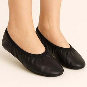 Könnte beinhalten: Ein Paar schwarze Ballerinas. Die Schuhe bestehen aus glattem, mattem Material mit runder Spitze und elastischem Besatz. Diese Ballerinas sind für Komfort und Flexibilität konzipiert.