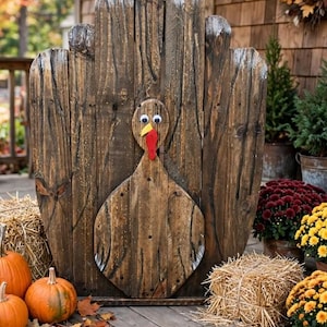 May include: A decorative turkey figure constructed from vertical dark brown wooden planks. The turkey features a circular head with two large googly eyes, a yellow triangular beak, and a red felt wattle. The body is rounded and attached to a fan-shaped tail.