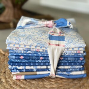 May include: A stack of folded fabric squares in various shades of blue, white, and tan, tied together with a strip of patterned cloth. The fabric features diverse prints including floral patterns, polka dots, and stripes with small pink accents.