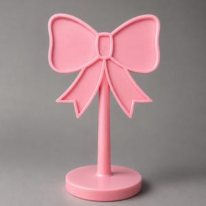 May include: A light pink stand featuring a decorative bow shape at the top. The object consists of a circular base, a vertical cylindrical stem, and a flat bow-shaped topper with raised edges, all constructed from a solid light pink material.