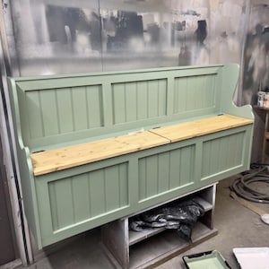 May include: A sage green wooden bench with a natural wood seat. The bench has a tall back and storage space beneath the seat. The bench is supported by a wooden frame. The bench is approximately 152 cm long.
