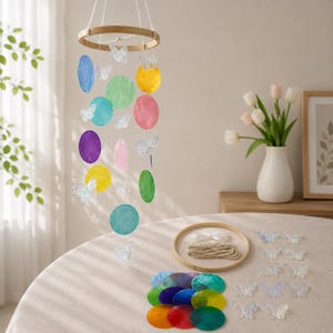May include: A hanging mobile featuring a circular wooden frame with dangling translucent butterfly shapes and colorful circular discs in shades of blue, green, yellow, pink, and purple. Additional loose butterfly pieces and a wooden ring are included.