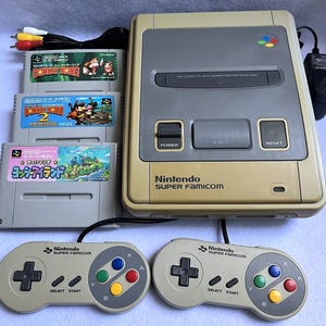 May include: A beige Nintendo Super Famicom game console with two grey controllers, three game cartridges including Super Donkey Kong, Donkey Kong 2, and Super Mario World 2: Yoshi's Island, a black power adapter, and a multi-coloured AV cable.