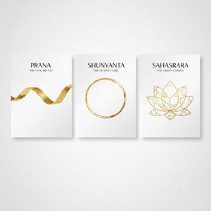 Puede incluir: Tres impresiones artísticas blancas con diseños dorados. La primera impresión dice "PRANA THE VITAL BREATH" con una cinta dorada. La segunda impresión dice "SHUNYANTA THE CREATIVE VOID" con un círculo dorado. La tercera impresión dice "SAHASRARA THE CROWN CHAKRA" con una flor de loto dorada.