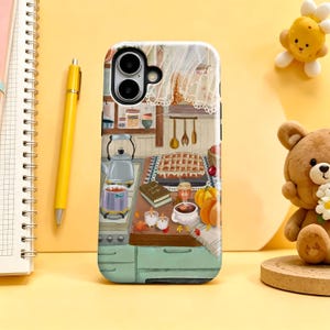 May include: A phone case featuring a detailed illustration of a cozy kitchen scene with a stove, a kettle, a pot, a baked pie, a book, pumpkins, and candles. The artwork displays warm autumn colors and kitchen utensils hanging on the wall.