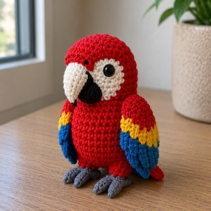 May include: A handmade crochet parrot in vibrant colors. The bird features a red body, a white and black beak, and wings with yellow and blue accents. The parrot has gray feet and a friendly, round appearance, perfect for a child's toy or home decor.