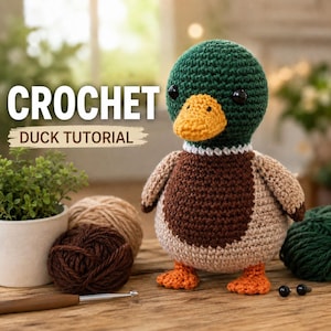 May include: A crocheted mallard duck toy with a dark green head, orange beak, white neck ring, brown chest, and light brown body. The text CROCHET DUCK TUTORIAL is visible. Nearby are yarn balls, a crochet hook, and two small black safety eyes.