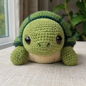 May include: A handmade crochet turtle in shades of green and beige. The turtle has large, black safety eyes and a smiling face. The shell is a darker green, and the body is a lighter green and beige. This soft toy is perfect for children.