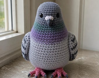 May include: A crocheted pigeon figurine featuring a rounded body with light gray yarn, a purple and green iridescent neck section, dark gray wing markings, black plastic eyes, a small white cere, a dark beak, and textured pink feet.
