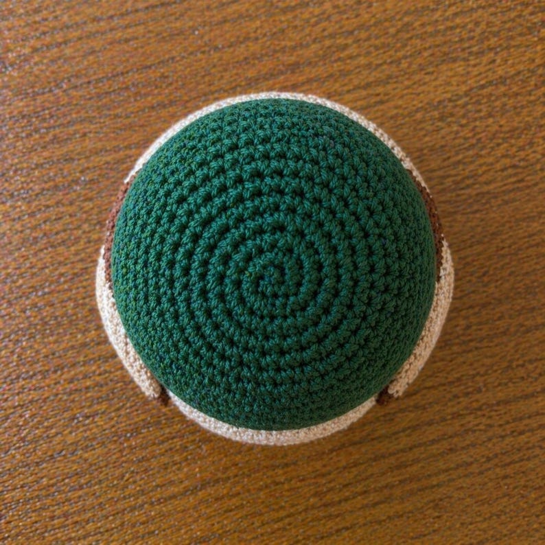 May include: A circular crochet coaster featuring a dark green center with a spiral stitch pattern, surrounded by a thick, light beige border. The item is constructed from yarn with a visible, textured, and dense looped stitch throughout the surface.