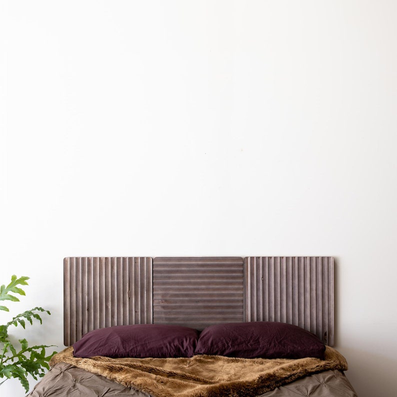 May include: A bed with a brown faux fur throw and two burgundy pillows. The headboard is made of three wooden panels with vertical slats.
