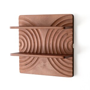 May include: A wooden wall shelf with two shelves. The shelf has a unique design with concentric circles carved into the wood. The shelf is a dark brown color.