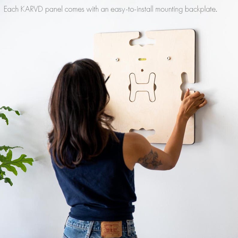 May include: A person installing a light wood wall-mounted panel with a cutout in the shape of the letter "H".