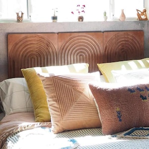 May include: A wooden headboard with a curved design, featuring three panels. The headboard is decorated with a variety of pillows, including a yellow velvet pillow, a brown pillow with a geometric pattern, and a brown pillow with a woven design.