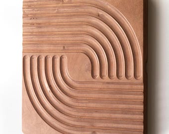 May include: A wooden wall art piece with a geometric design of concentric circles carved into the surface. The wood is a light brown color.