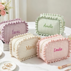 Puede incluir: Cuatro neceseres de maquillaje con estampado de cuadros en colores pastel: lavanda, verde, crema y rosa. Cada neceser tiene un borde con volantes y una cremallera dorada. Los neceseres están personalizados con los nombres bordados: Lucas, Amelie, Mavis y Emilia.