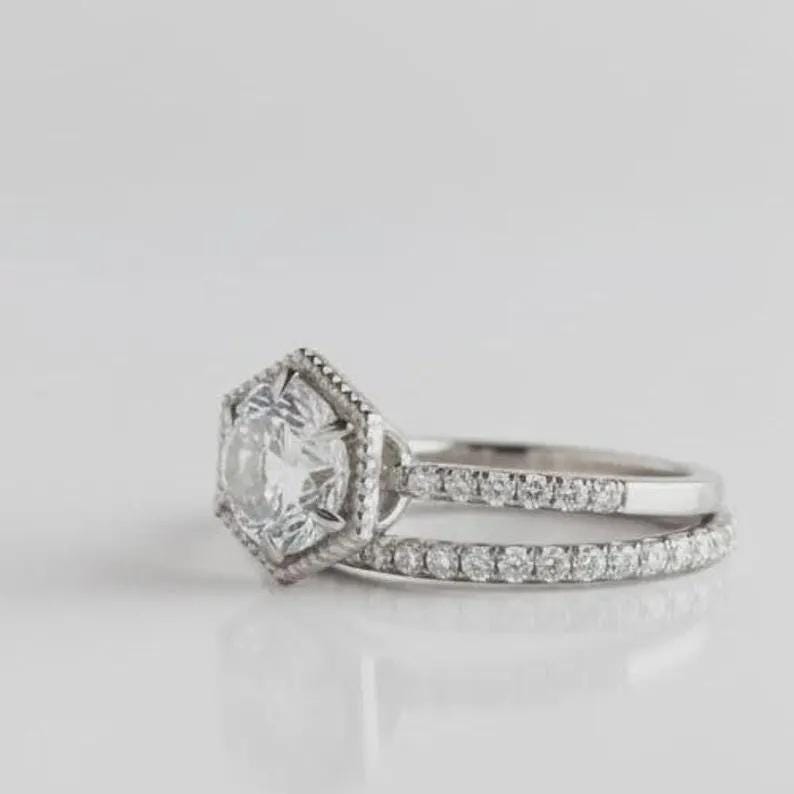 May include: A silver-toned ring featuring a central round gemstone set within a hexagonal frame. The band is split into two distinct sections, with the lower band and the upper section of the hexagonal setting adorned with small, clear, round stones.