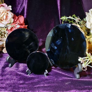May include: Three black, round, reflective objects of varying sizes are displayed on small stands against a purple velvet backdrop. The objects appear to be polished and have a glossy finish. Floral arrangements are visible in the background.