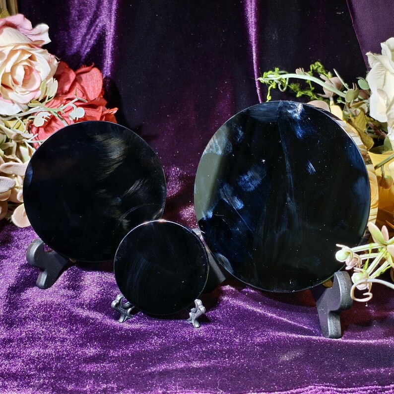 May include: Three black, round, reflective objects of varying sizes are displayed on small stands against a purple velvet backdrop. The objects appear to be polished and have a glossy finish. Floral arrangements are visible in the background.