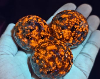 Può includere: Tre oggetti sferici con una superficie ruvida e craterizzata. Le sfere presentano un colore di base scuro con motivi maculati arancioni e gialli vivaci e luminosi su tutto l'esterno, creando un aspetto ad alto contrasto e brillante.