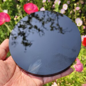 May include: A round, black, reflective object is held in a hand. The object's surface reflects the sky and tree branches. The background features pink and white flowers.