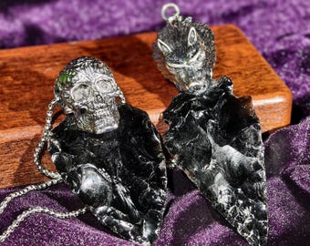 May include: Two pendants featuring black obsidian-like stone arrowheads. One pendant has a silver-toned metal skull topper, and the other has a silver-toned metal wolf head topper. Both pendants include a silver-toned metal chain link necklace.