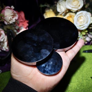 May include: Three black, circular objects with a reflective surface are held in a hand. The objects vary in size, with the largest at the top and the smallest at the bottom. The background features flowers.