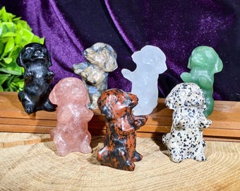 Può includere: Una collezione di sette piccole statuette di cani scolpite in vari colori e materiali. I cani sono in piedi, alcuni sembrano essere fatti di pietra o cristallo. I colori includono nero, rosa, verde e motivi maculati.