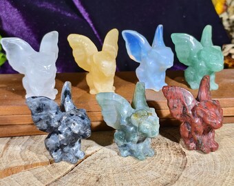 Può includere: Una collezione di sette figurine di cristallo scolpite, ognuna raffigurante una creatura alata. Le figurine variano di colore, tra cui trasparente, giallo, blu, verde, grigio e rosso. Sono esposte su una superficie di legno.