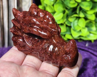 Può includere: Una scultura a forma di testa di drago scolpita in una tonalità rosso intenso. La scultura presenta squame dettagliate, un muso prominente e un occhio chiuso. La testa di drago è un oggetto decorativo, forse per l'esposizione o la collezione.