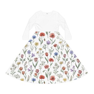 Könnte beinhalten: Ein langärmeliges Kleid mit einem einfarbigen weißen Oberteil und einem ausgestellten Rock mit buntem Blumenmuster. Der Rock zeigt ein Muster aus roten Mohnblumen, blauen Kornblumen, gelben Gänseblümchen und grünem Blattwerk auf weißem Grund.
