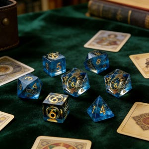 May include: A collection of blue and gold dice with various shapes and numbers, including six-sided cubes, and multi-sided dice. The dice are scattered on a dark green velvet surface, with playing cards visible in the background. The dice have gold numbering and decorative elements.