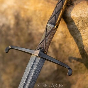 Puede incluir: Una espada con una hoja de acero de Damasco estampada y una guarda de metal oscuro. El mango presenta una empuñadura texturizada y envuelta con un pomo ensanchado. El texto STEEL ARIES está impreso en la hoja cerca de la guarda, mostrando metalurgia.