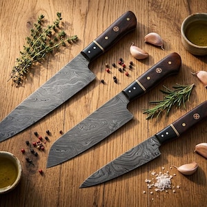 Könnte beinhalten: Drei Küchenmesser aus Damaszenerstahl mit Holzgriffen liegen auf einer Holzoberfläche. Die Messer werden von Knoblauchzehen, Kräutern, Gewürzen und einer kleinen Schüssel Öl begleitet. Die Klingen haben ein ausgeprägtes Muster.