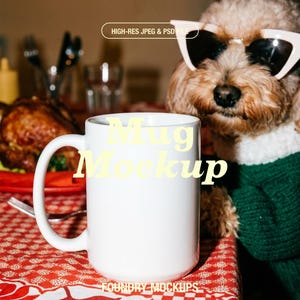 May include: A white ceramic mug with a large handle sits on a red and white floral tablecloth. The text "Mug Mockup" is printed on the mug. A dog wearing sunglasses and a green sweater is in the background.