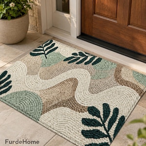 Può includere: Un zerbino rettangolare con un design botanico. Il tappeto presenta uno sfondo color crema con motivi intrecciati nelle tonalità del verde, marrone e bianco. Forme di foglie verde scuro sono sparse sulla superficie. Il marchio "FurdeHome" è visibile.