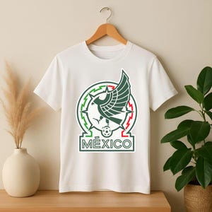 Peut inclure: T-shirt blanc avec l'embl&egrave;me de l'&eacute;quipe nationale mexicaine. L'embl&egrave;me comprend un cercle vert et rouge avec un aigle central, un ballon de football et le mot "M&Eacute;XICO" dans un rectangle.