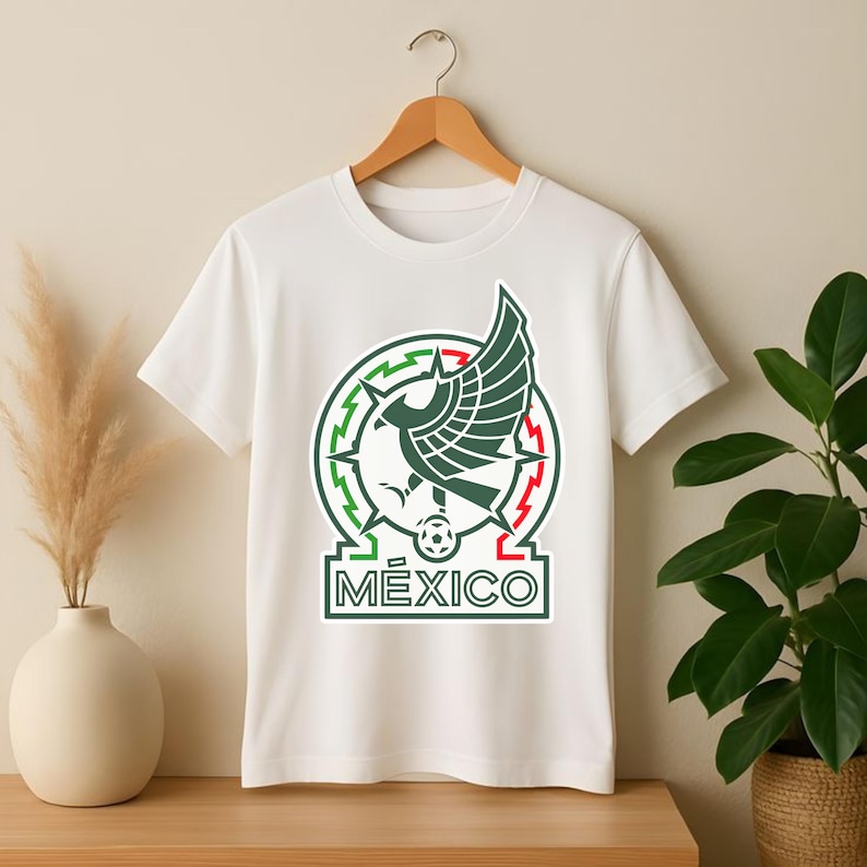Peut inclure: T-shirt blanc avec l'embl&egrave;me de l'&eacute;quipe nationale mexicaine. L'embl&egrave;me comprend un cercle vert et rouge avec un aigle central, un ballon de football et le mot "M&Eacute;XICO" dans un rectangle.