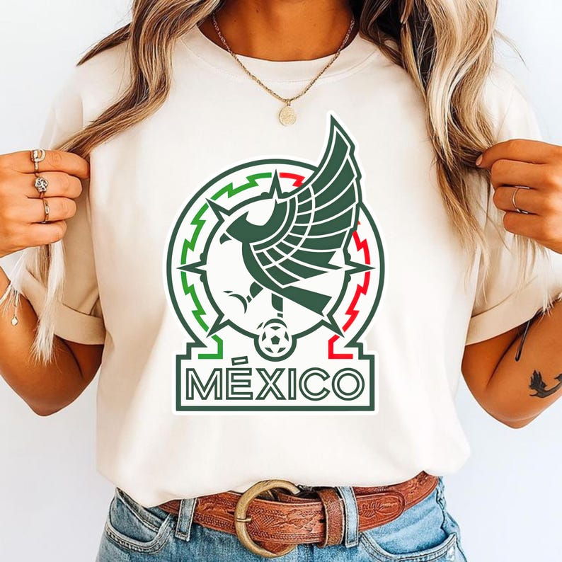 Peut inclure: T-shirt cr&egrave;me avec l'embl&egrave;me national mexicain. L'embl&egrave;me comprend un motif circulaire vert et rouge avec un aigle stylis&eacute;, un ballon de football et le mot "M&Eacute;XICO" en vert. Le t-shirt est port&eacute; par une personne.